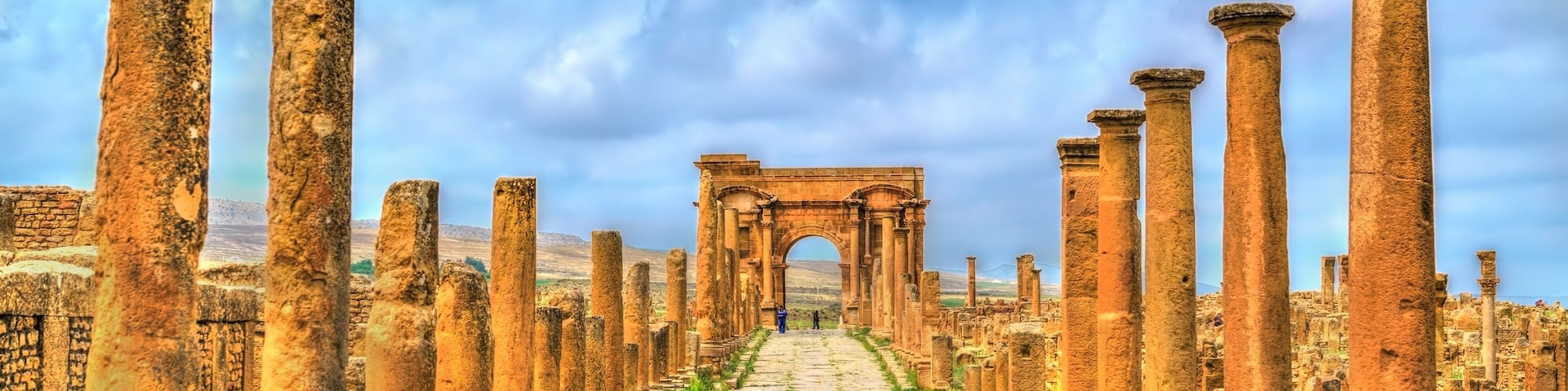 Ancient ruins with columns and an archway leading into the distance.