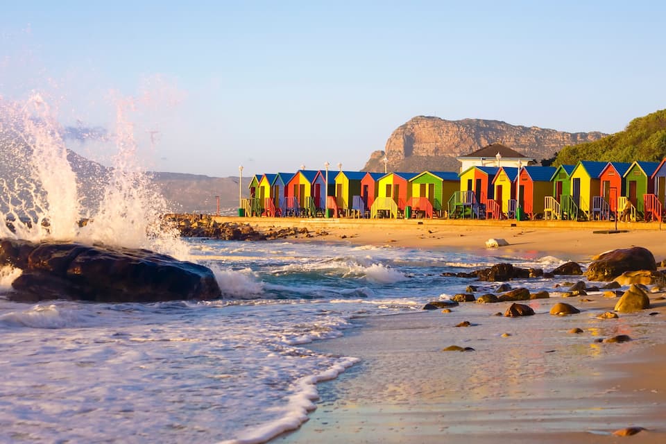 A beach with colorful beach huts and waves crashing onto the shore.