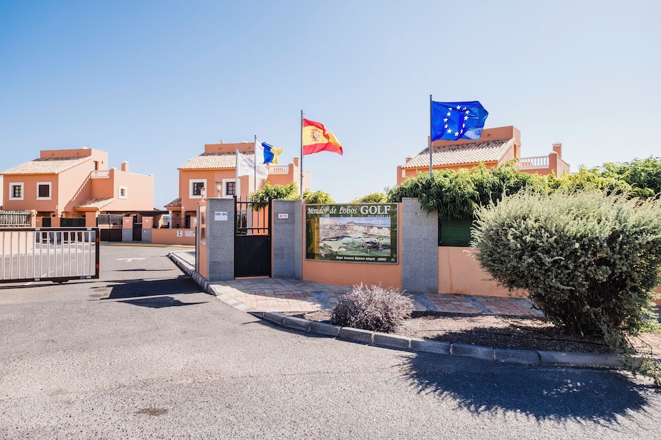 Entrada a un campo de golf con banderas, un cartel y edificios.