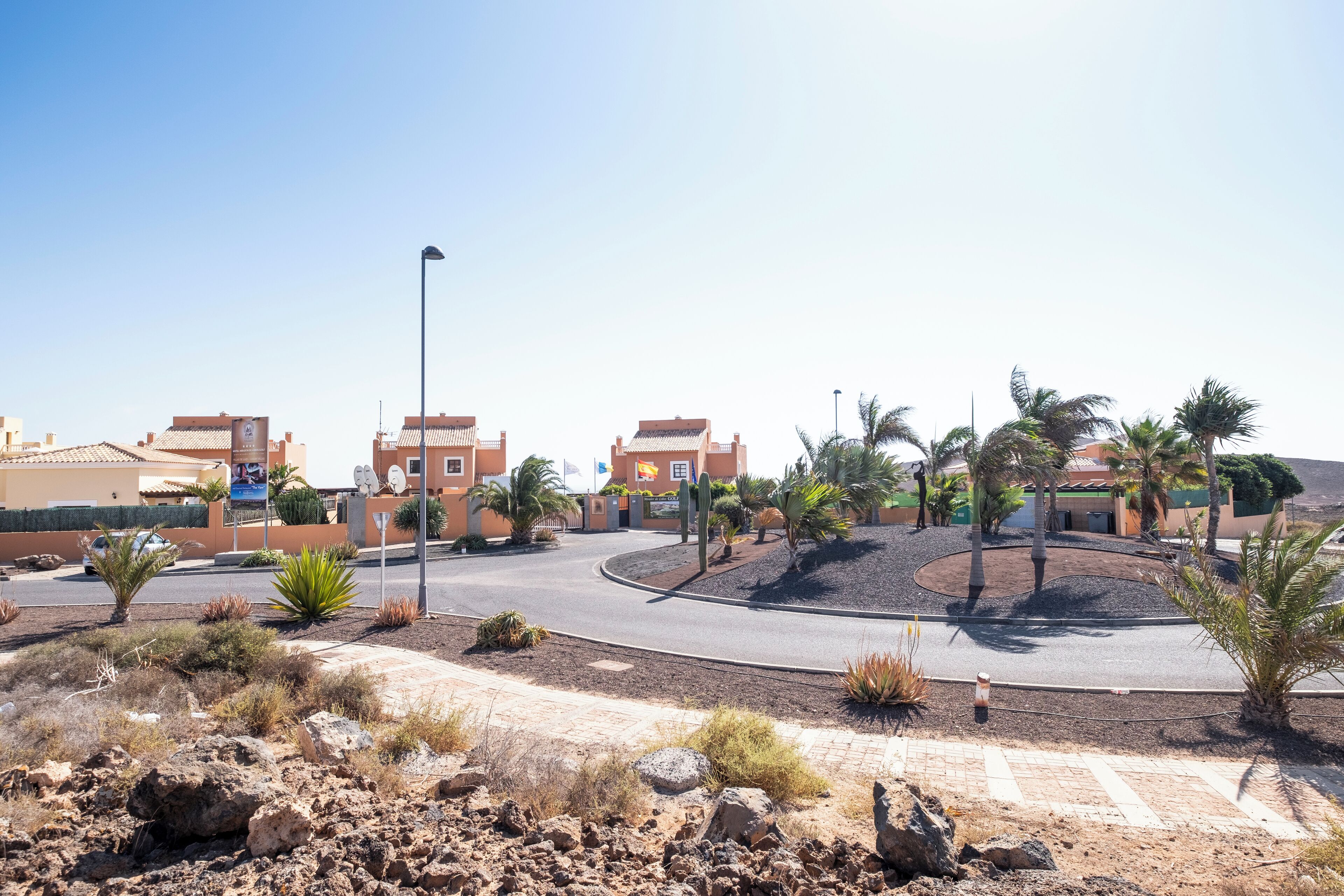 A desert landscape with a roundabout, palm trees, and buildings with red-tiled roofs.
