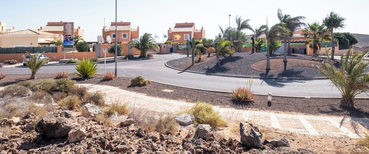 A desert landscape with a roundabout, palm trees, and buildings with red-tiled roofs.