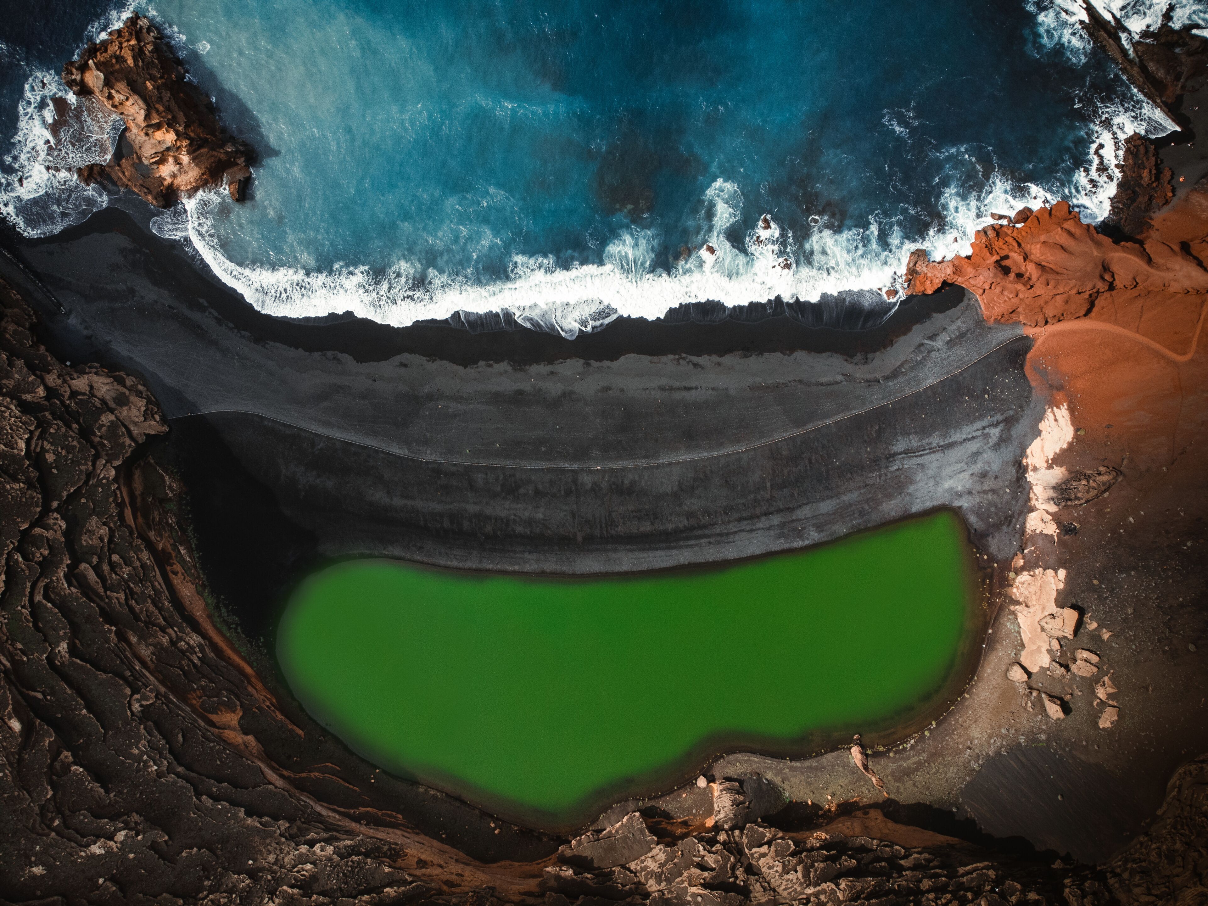 Aerial view of the El lago Verde (Lanzarote) - green lagoon with blue ocean - top view. Blue Atlantic ocean with waves and black sand beach in Lanzarote by drone.