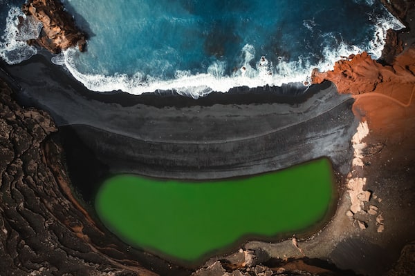 Aerial view of the El lago Verde (Lanzarote) - green lagoon with blue ocean - top view. Blue Atlantic ocean with waves and black sand beach in Lanzarote by drone.