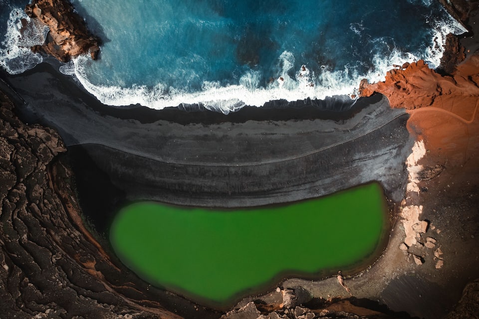 Paisagem costeira com uma lagoa verde, linha de costa rochosa e ondas quebrando nas pedras.