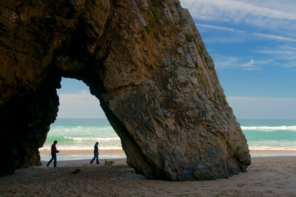 A large rock formation with a natural arch on a beach.
