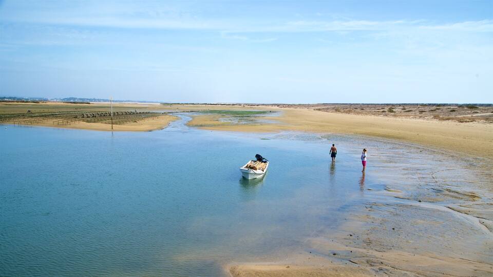 A boat on a calm river with people standing on the shore.
