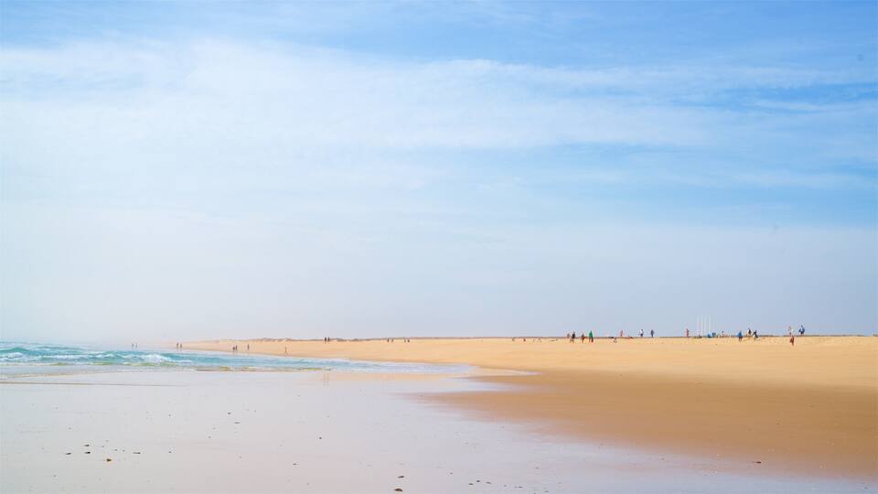 A wide sandy beach with gentle waves and a clear sky.