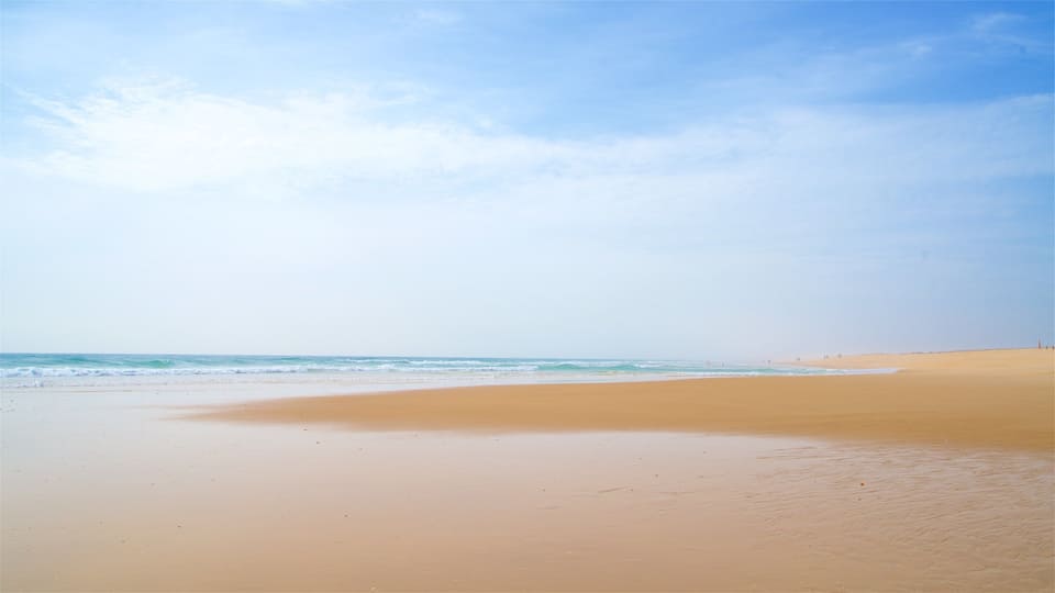A wide sandy beach with gentle waves and a clear sky.