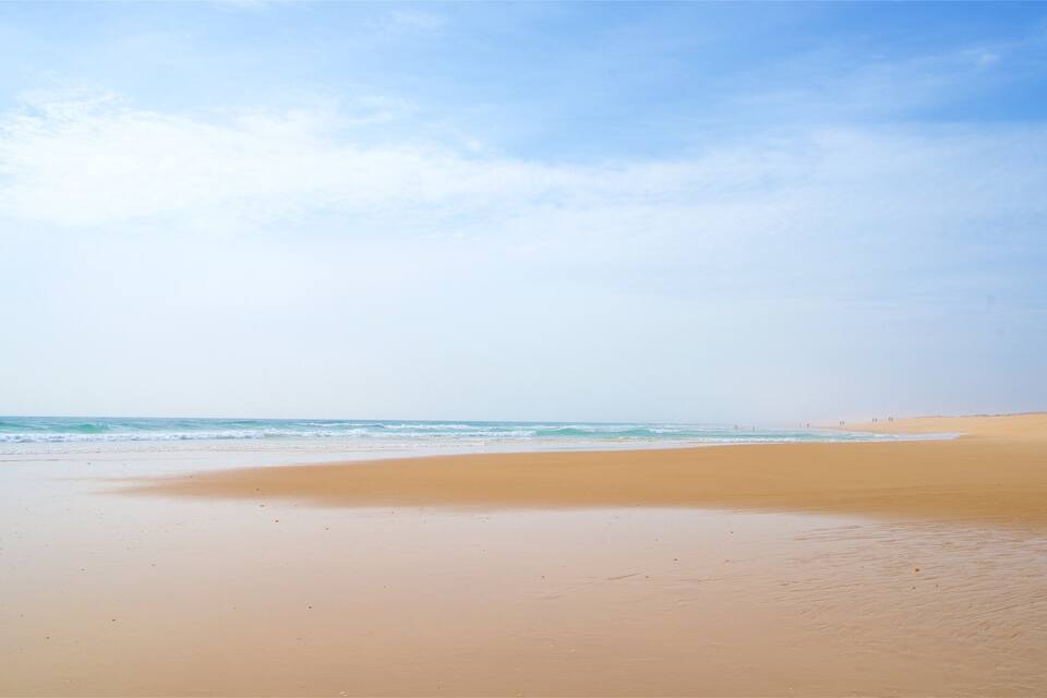 A wide sandy beach with gentle waves and a clear sky.