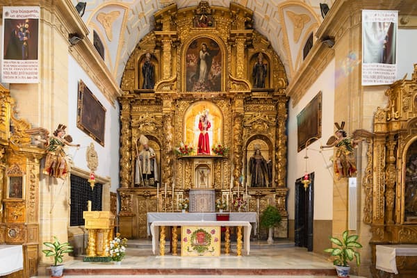 L’intérieur d’une église richement décorée, orné de motifs dorés, avec un autel central et des statues religieuses.