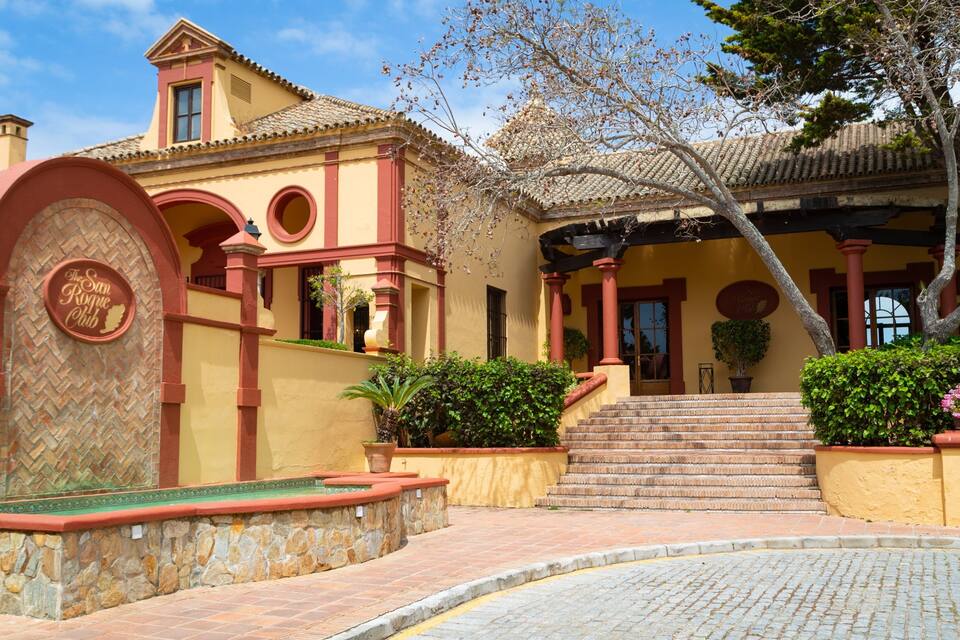 Un edificio con fachada amarilla, arcos rojos y un muro de piedra.