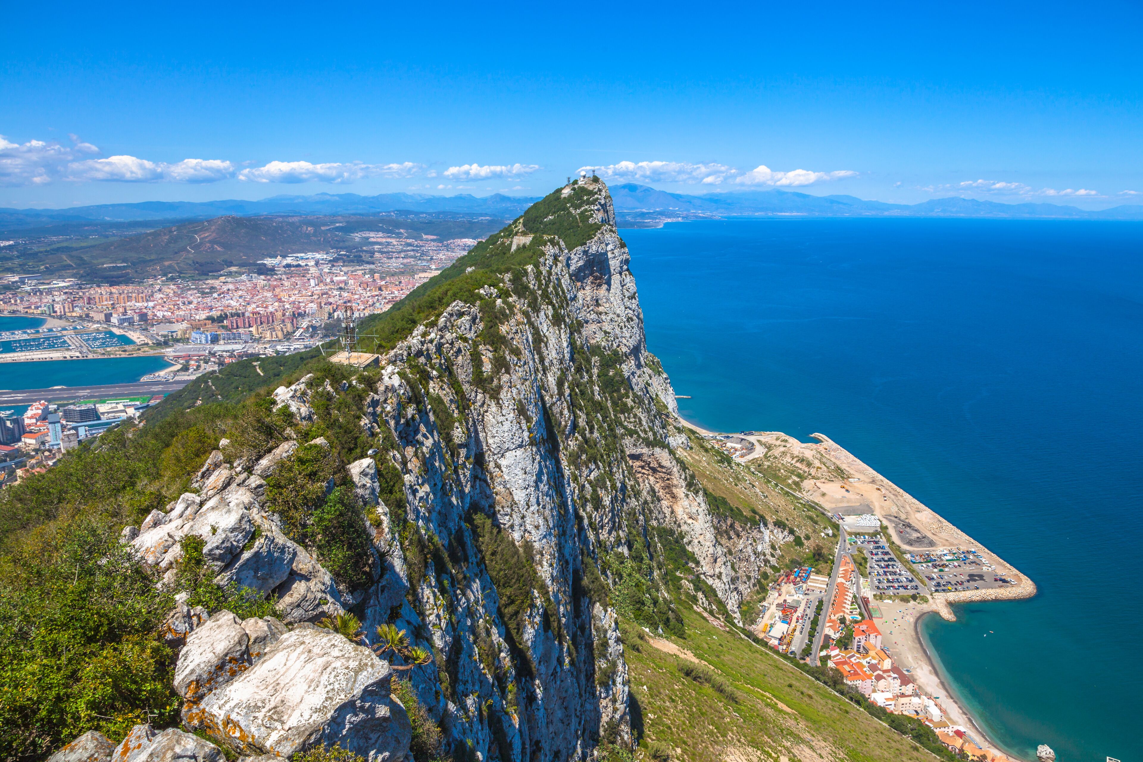 Aerial view of top of Gibraltar Rock, in Upper Rock Natural Reserve: on the left Gibraltar town and bay, La Linea town in Spain at the far end, Mediterranean Sea on the right. United Kingdom, Europe.