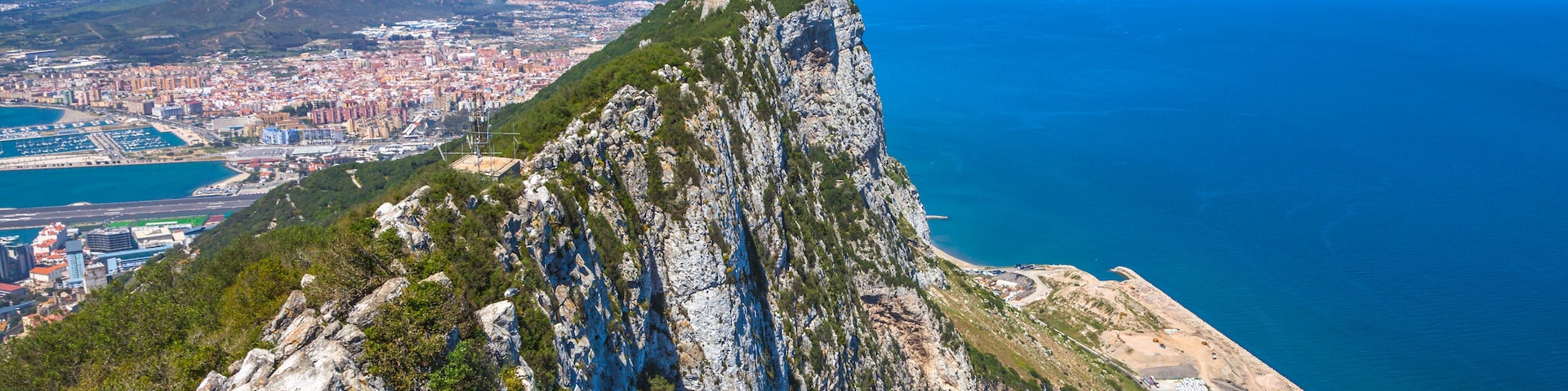 Aerial view of top of Gibraltar Rock, in Upper Rock Natural Reserve: on the left Gibraltar town and bay, La Linea town in Spain at the far end, Mediterranean Sea on the right. United Kingdom, Europe.