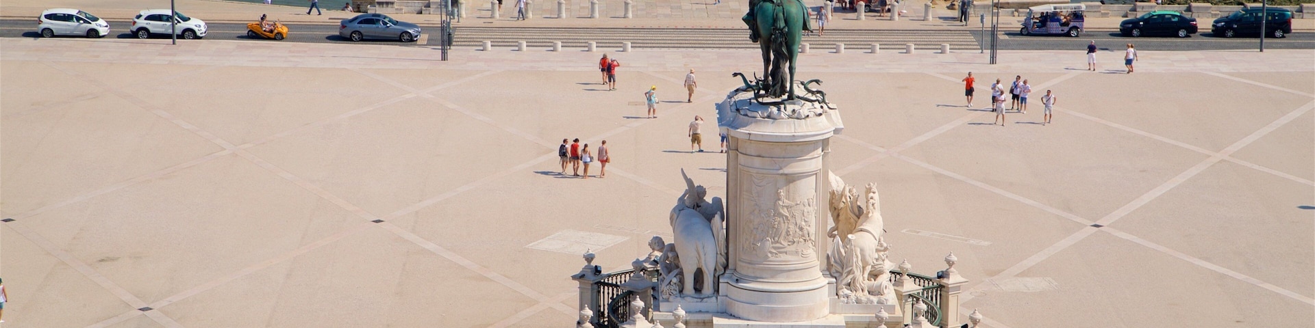 Uma grande praça aberta com uma estátua central, cercada por um muro baixo e escadas que levam a ela.