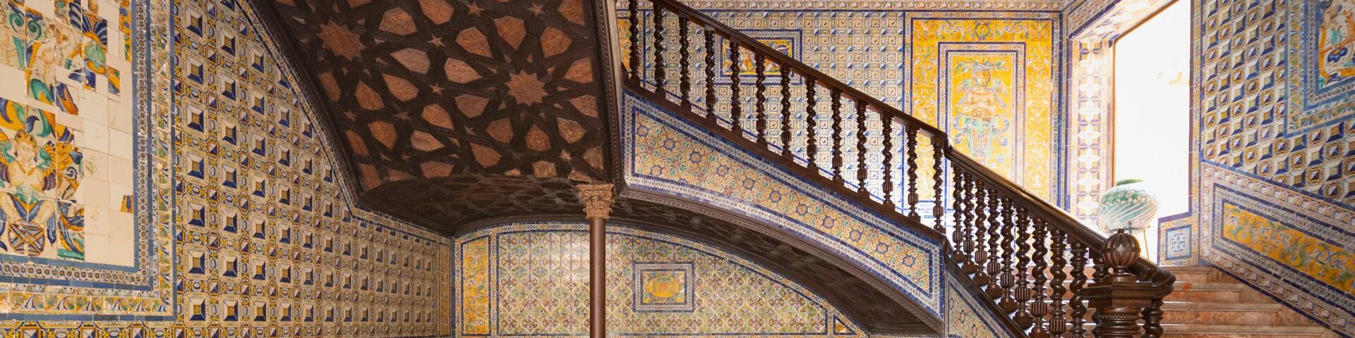 Una majestuosa escalera con elaborados trabajos en mosaico y un jarrón grande en el suelo.