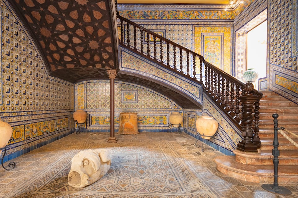 A grand staircase with intricate tile work and a large vase on the floor.