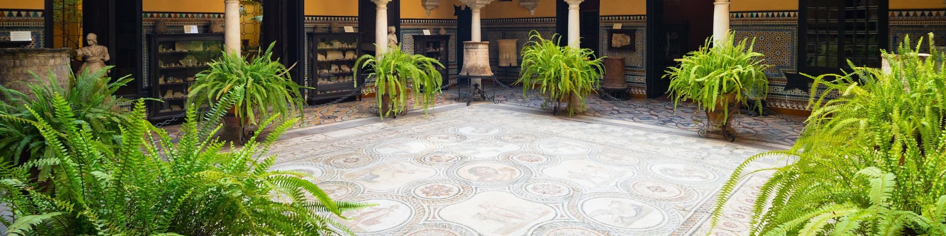 Un patio con arcos ornamentales, suelo de baldosas y abundante vegetación.