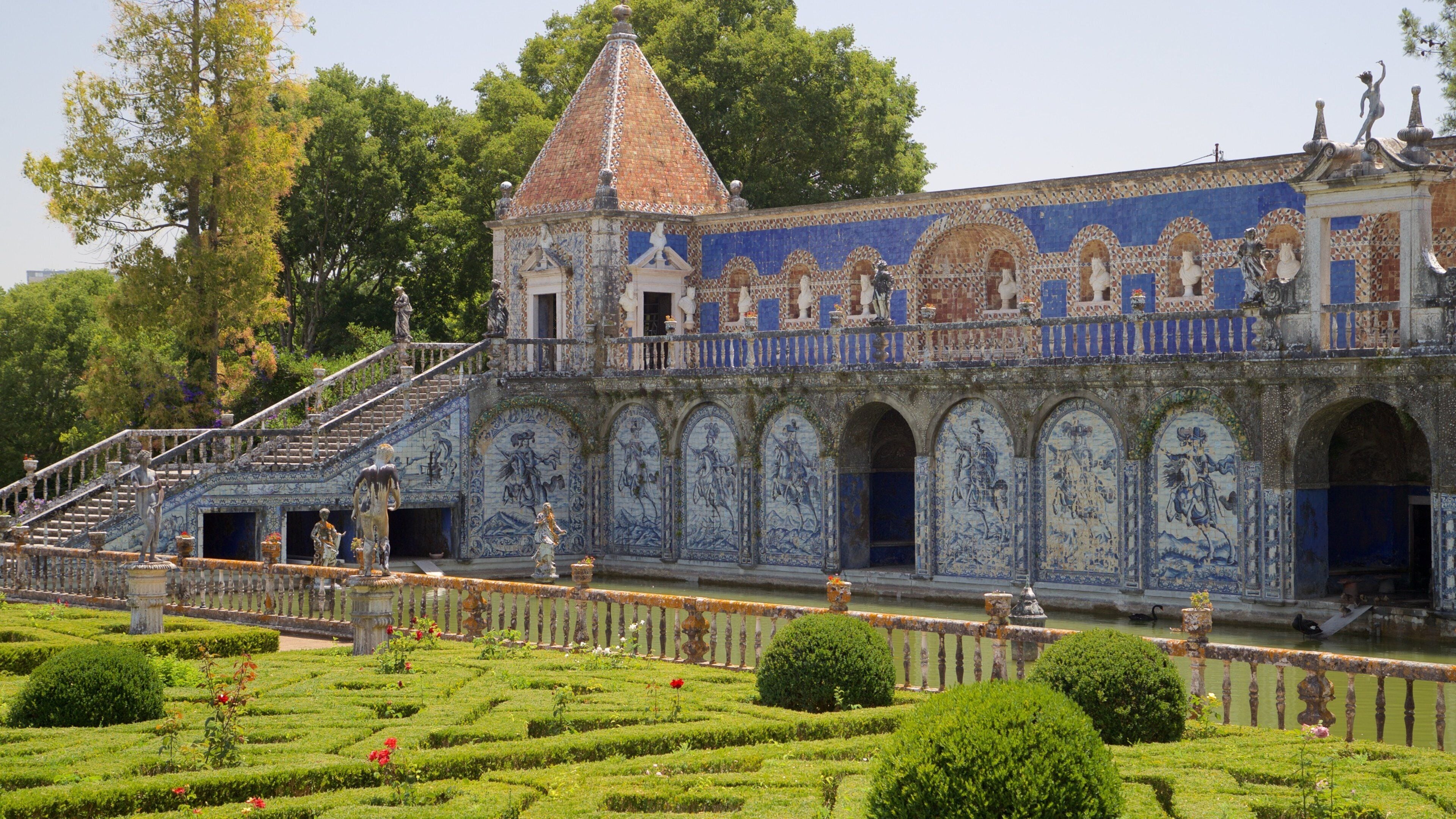 Un edificio histórico con intrincados trabajos de azulejos azules y blancos, una torre destacada y un jardín cuidado con setos y flores.