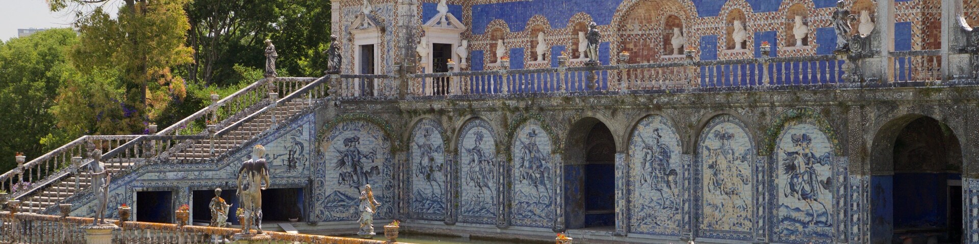 Un edificio histórico con intrincados trabajos de azulejos azules y blancos, una torre destacada y un jardín cuidado con setos y flores.