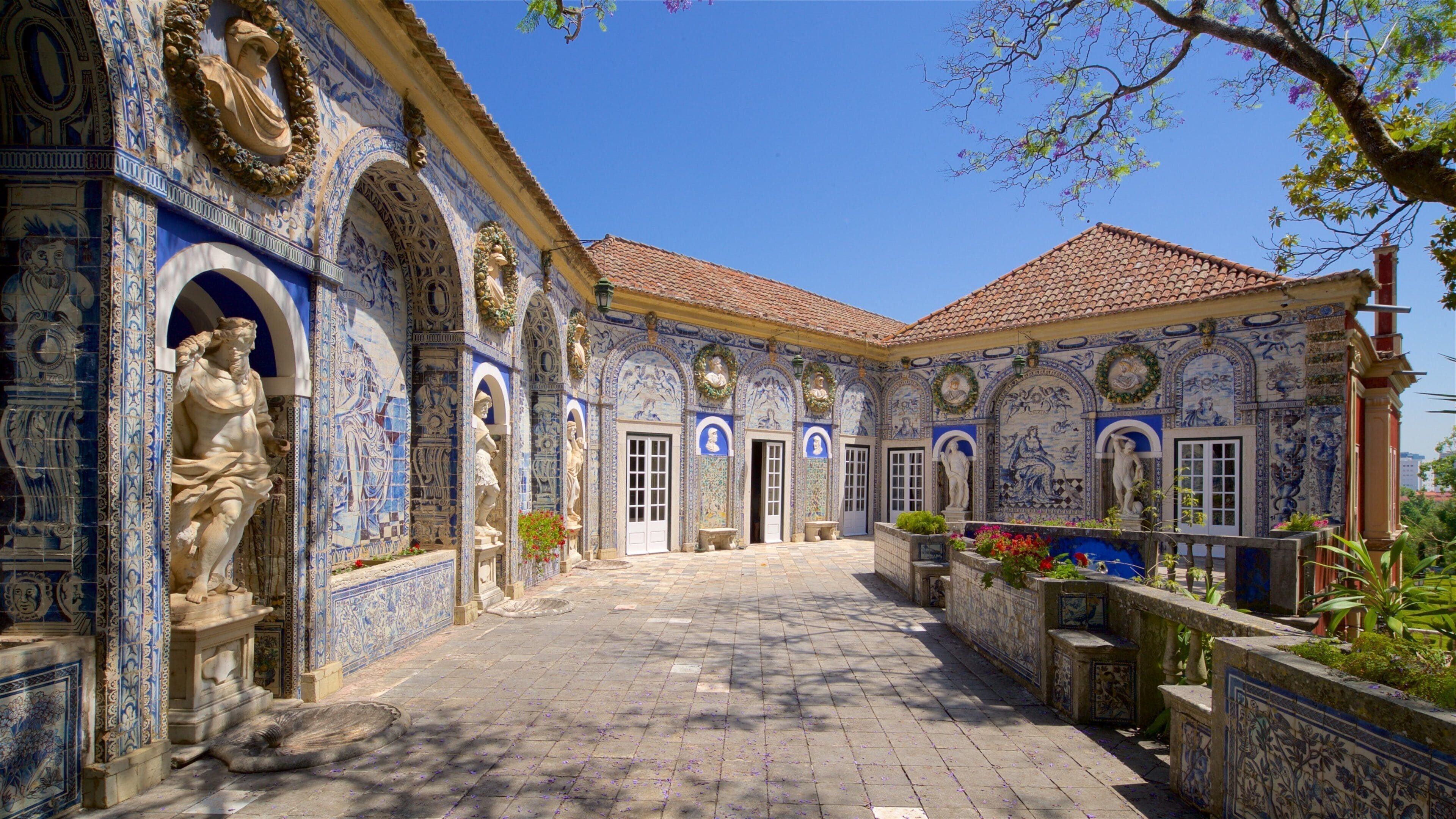 A courtyard with blue and white tiled walls, statues, and a tiled roof.