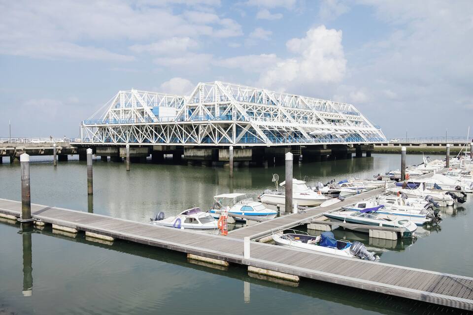 Un port de plaisance avec des bateaux amarrés et, au fond, une grande structure de pont blanc.