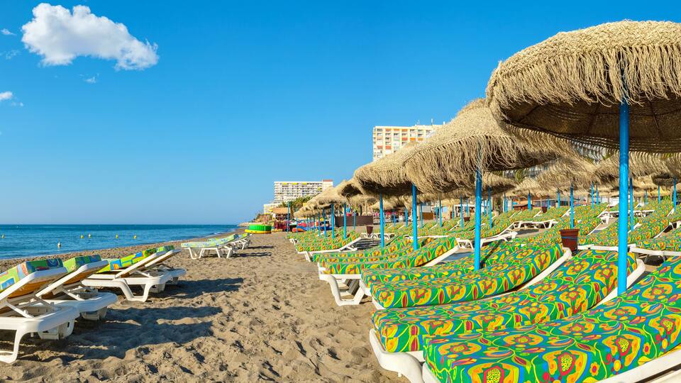 A beach with rows of colorful lounge chairs and thatched umbrellas.