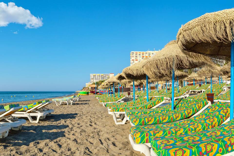 Une plage bordée de rangées de chaises longues colorées et d’ombrelles en chaume.