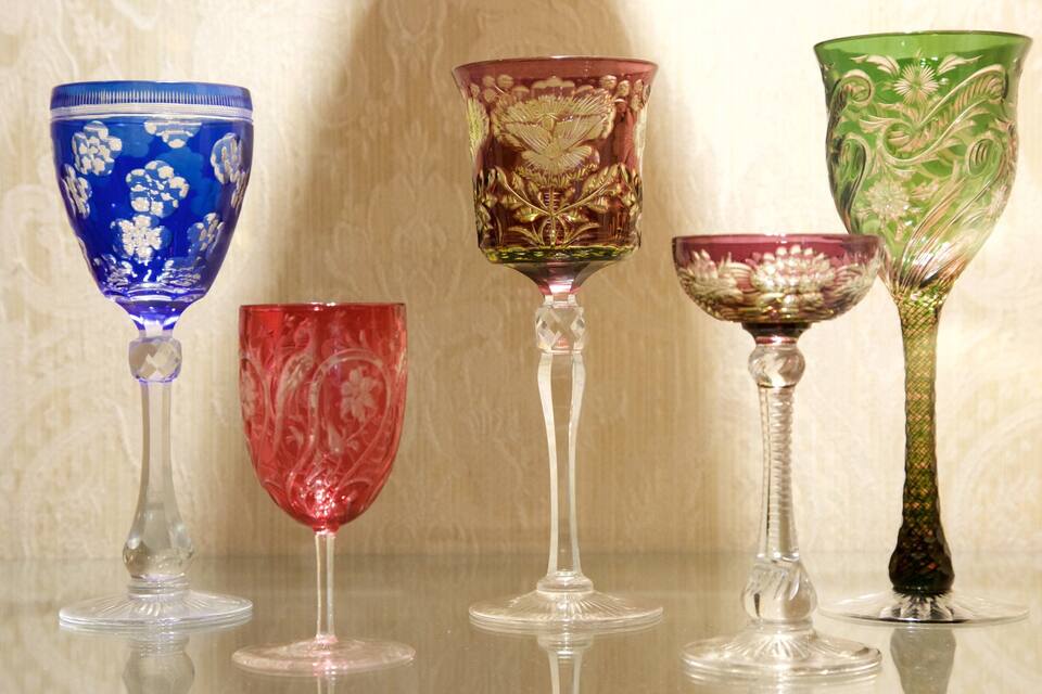 Five glassware items with intricate designs on a reflective surface.