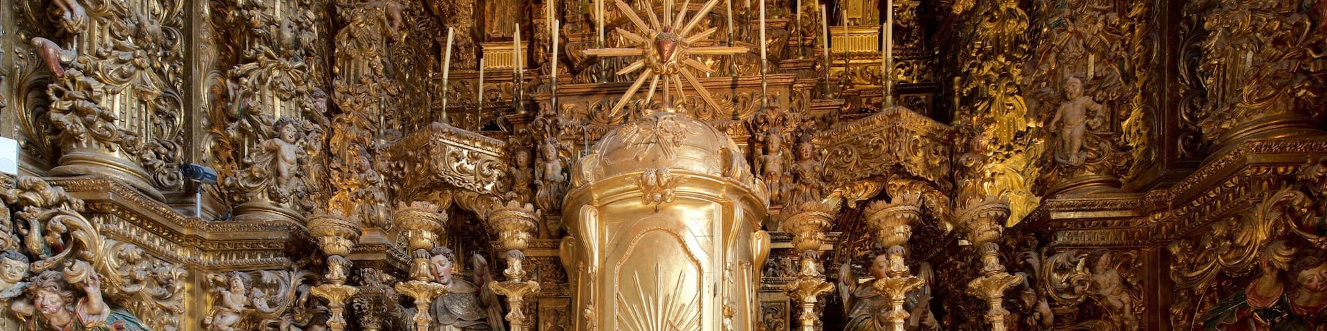 Un interior religioso ornamentado con un crucifijo central, detalles dorados y esculturas elaboradas.
