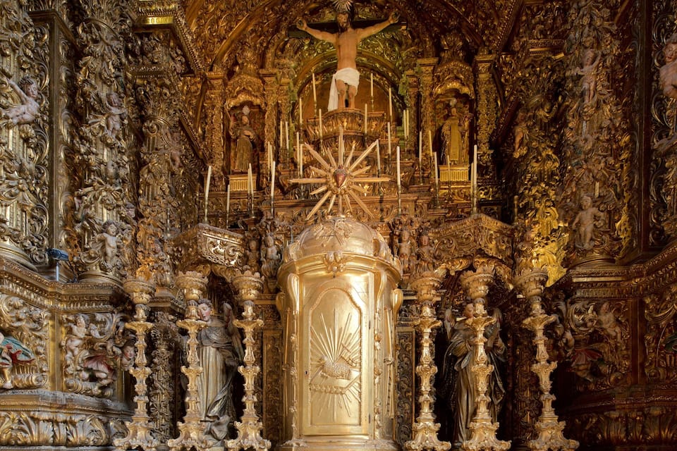 An ornate religious interior with a central crucifix, golden decorations, and detailed sculptures.