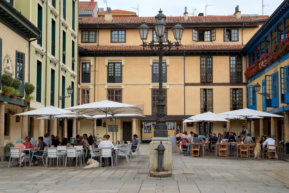 A courtyard with outdoor seating, a fountain, and buildings with balconies and flower boxes.