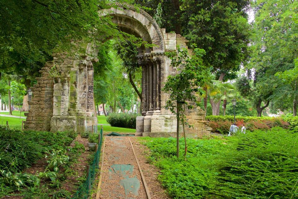 Un antiguo arco de piedra rodeado de vegetación exuberante y un camino de jardín cuidado.