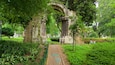 An ancient stone archway surrounded by lush greenery and a well-maintained garden path.