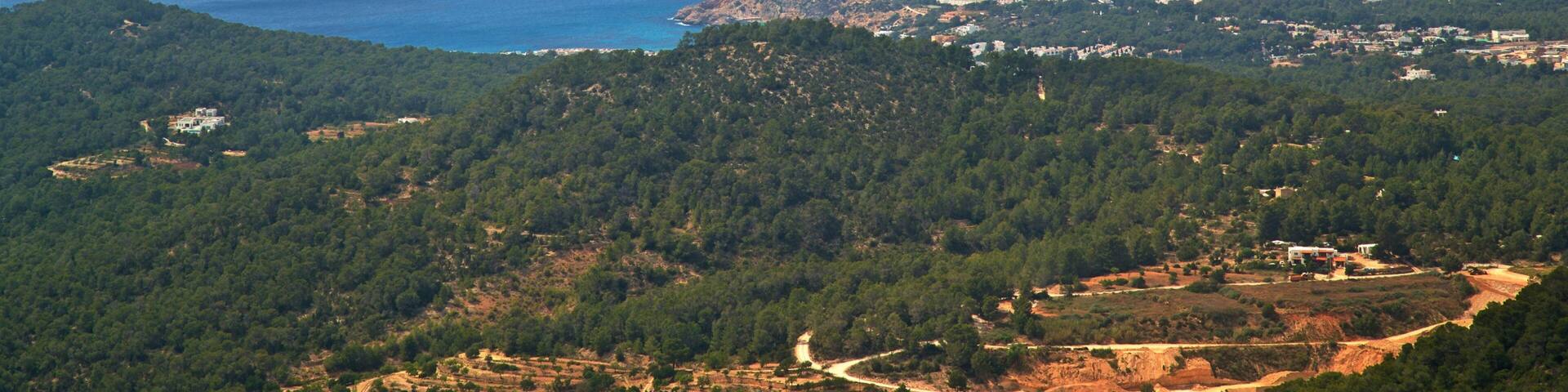 Un pueblo costero con colinas densamente arboladas, una vista despejada del mar y varias islas pequeñas en la distancia.