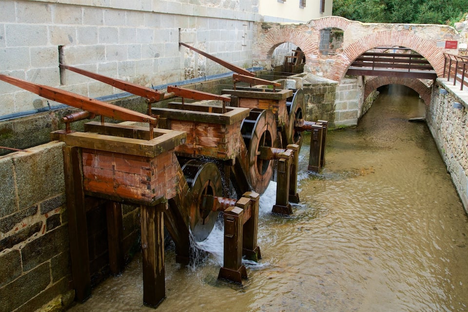 A historical watermill with wooden machinery and a stone bridge in the background.