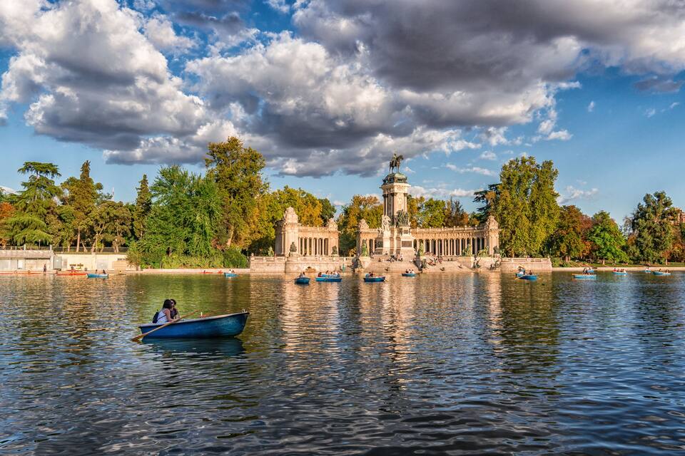 Ein ruhiger See mit Booten, einer Statue und einem klassizistischen Gebäude im Hintergrund.