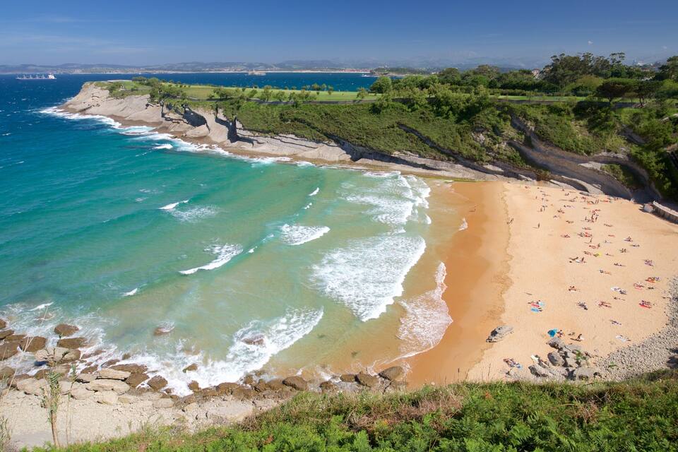A coastal beach with clear turquoise waters, sandy shore, and rocky cliffs.