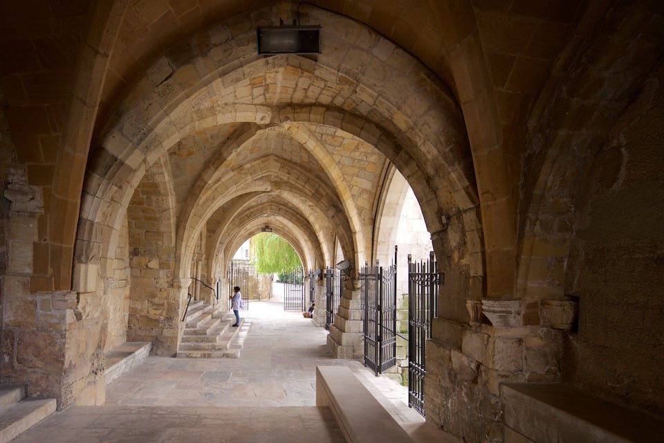 A stone corridor with arches, a staircase, and a gate.
