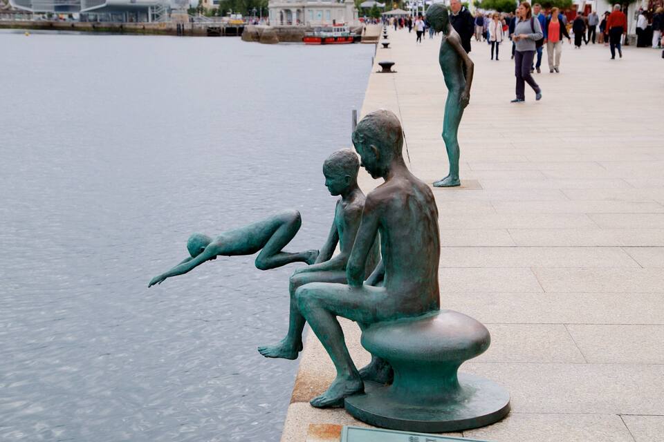 A bronze sculpture of a child and an adult by a waterfront.