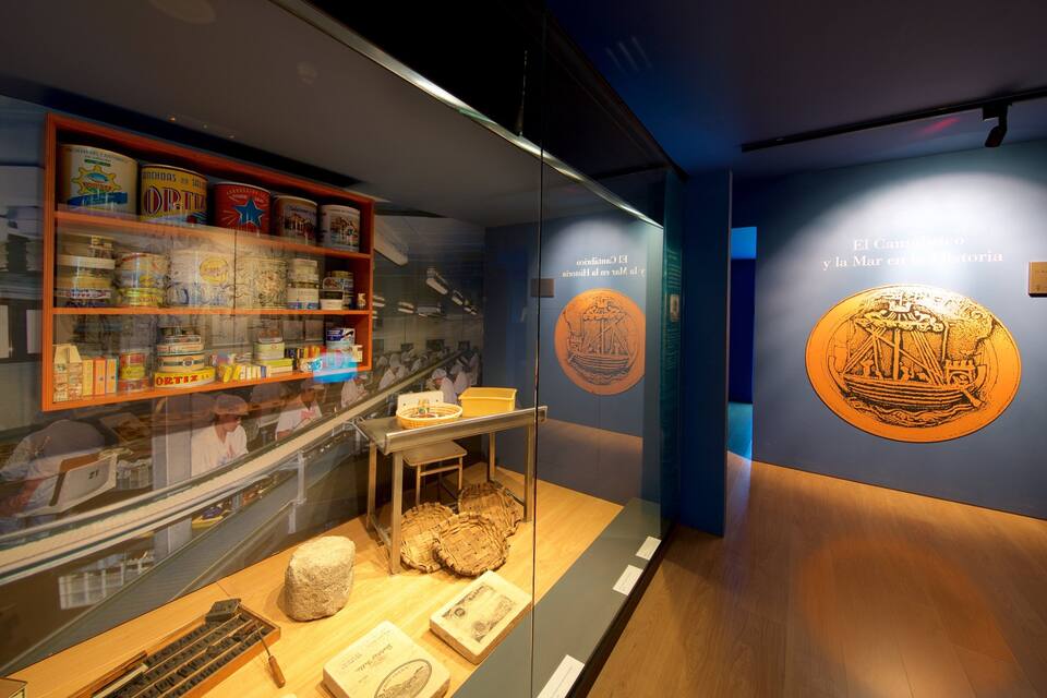 Una exhibición de museo con artefactos históricos, incluyendo recipientes de comida y una vitrina con objetos.