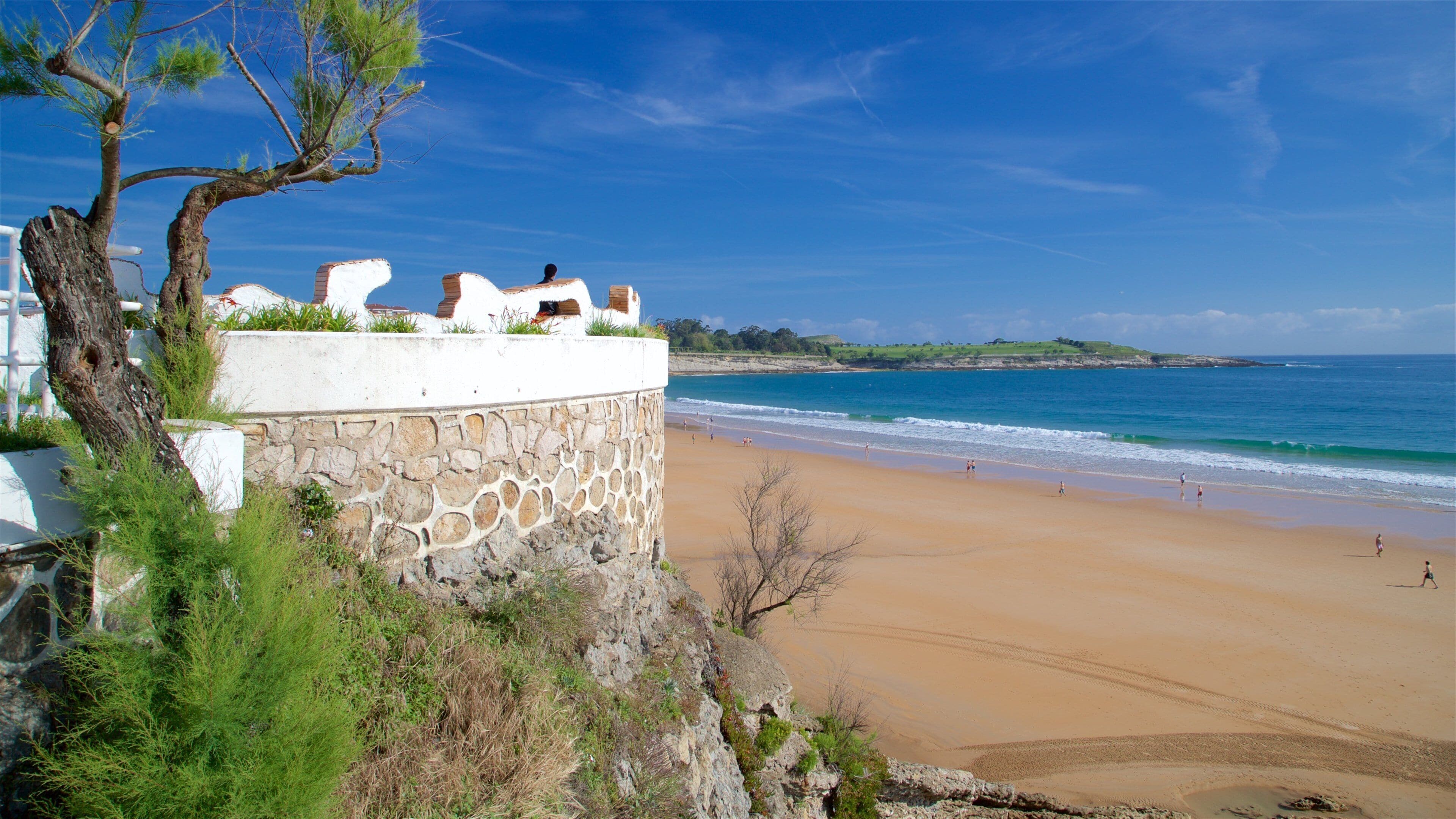 Paisatge costaner amb mur de pedra, platja i oceà.