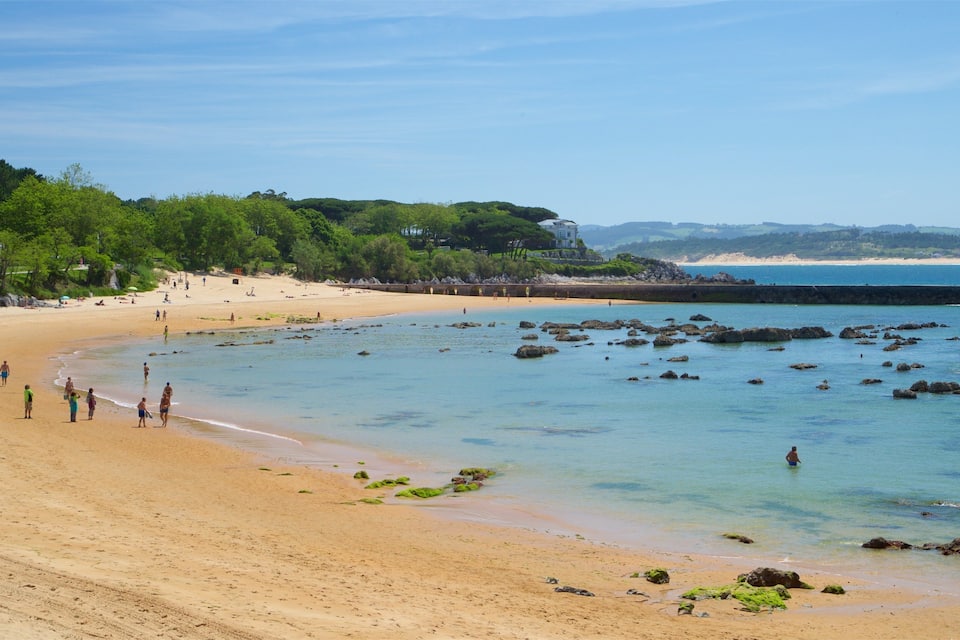 A sandy beach with clear water, rocks, and people.