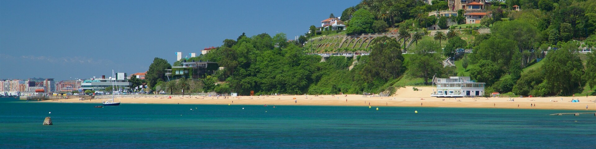 Un paisaje costero con playa, un edificio grande en una colina y un cielo azul despejado.