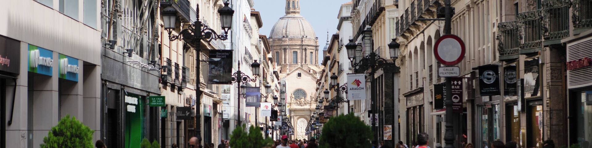 A bustling urban street with historic buildings, a prominent dome, and pedestrians.
