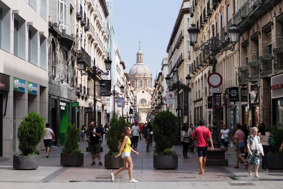 A bustling urban street with historic buildings, a prominent dome, and pedestrians.