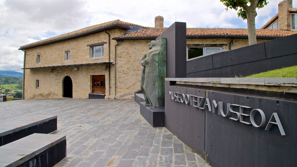A stone building with a tiled roof and a large sculpture in front.