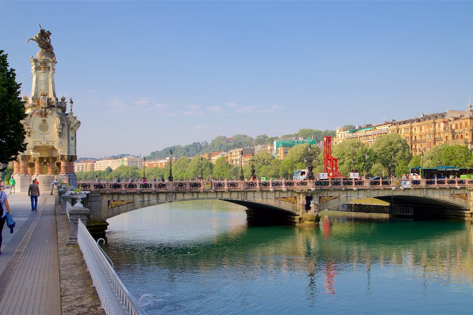 Ein Fluss mit einer Brücke, einer Statue und Gebäuden im Hintergrund.