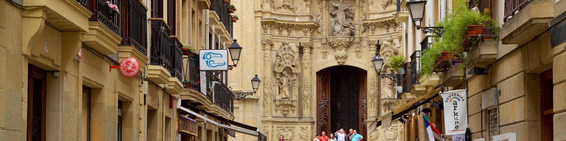Una calle estrecha con edificios ornamentados, una entrada imponente y gente caminando.
