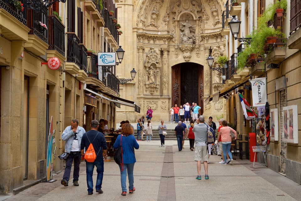 Una calle estrecha con edificios ornamentados, una entrada imponente y gente caminando.