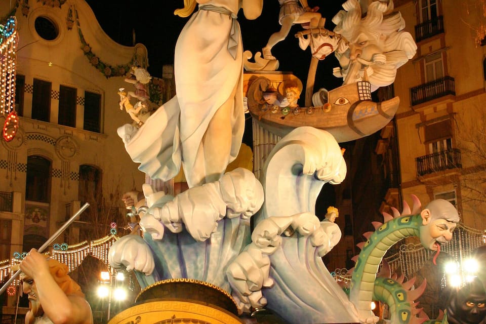Escultura ao ar livre à noite com diversas figuras e uma grande criatura semelhante a um dragão.